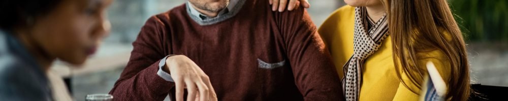 Mid adult couple analyzing mortgage agreement while being on a meeting with real estate agent. Focus is on woman pointing on a document.