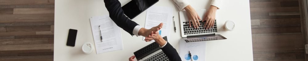 Top view of colleagues working together at laptops with handouts, coffee, devices around. Male worker giving high five to female associate during negotiations. Concept of success, teamwork, cooperation